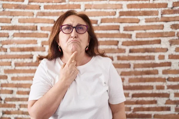 Mujer Mayor Con Gafas Pie Sobre Pared Ladrillos Pensando Concentrado —  Fotos de Stock