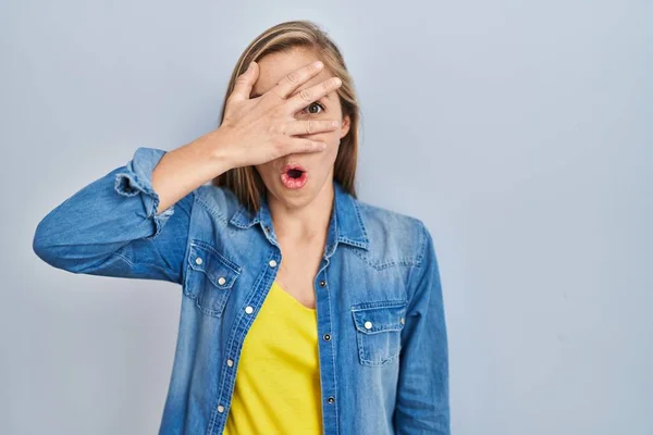 Young Blonde Woman Standing Blue Background Peeking Shock Covering Face — Stock Photo, Image