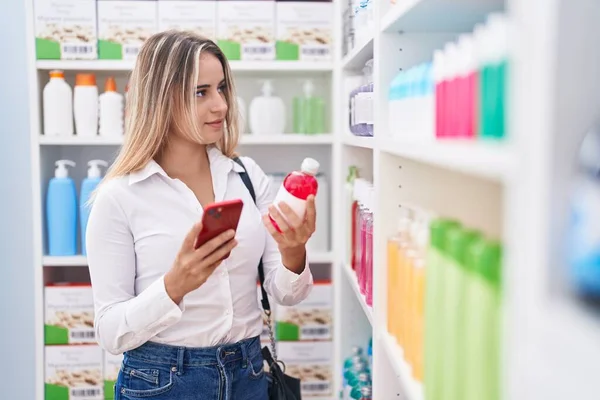 Young Blonde Woman Customer Using Smartphone Holding Medicine Bottle Pharmacy — 스톡 사진