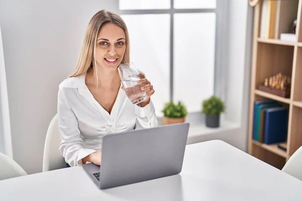 家のテーブルの上に座ってノートパソコンの飲料水を使用して若い女性 — ストック写真