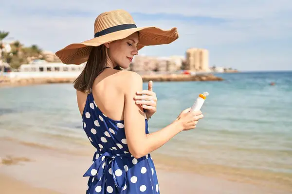 若いですブロンド女性観光客身に着けています夏の帽子適用日焼け止めオン腕でビーチ — ストック写真
