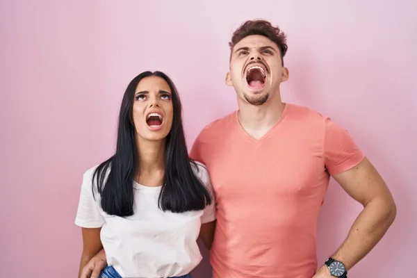 若いヒスパニック系のカップルピンクの背景に立って怒っていると怒っている不満と激怒叫び 怒りで叫んで 怒りと攻撃的な考え方 — ストック写真