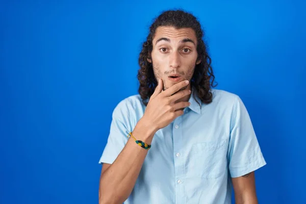 Junger Hispanischer Mann Steht Vor Blauem Hintergrund Und Schaut Fasziniert — Stockfoto