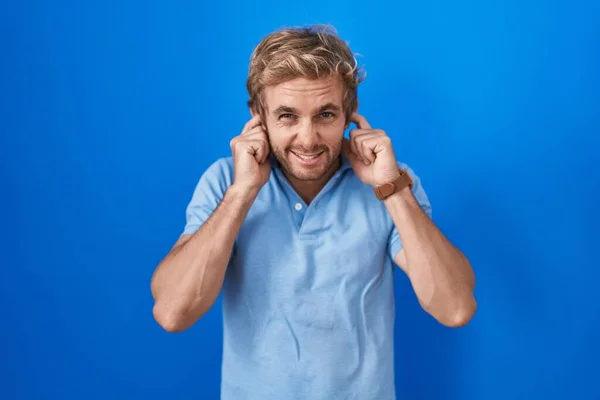 白人男子站在蓝色的背景之上 用手指捂住耳朵 对嘈杂的音乐表示恼怒的表情 聋人概念 — 图库照片