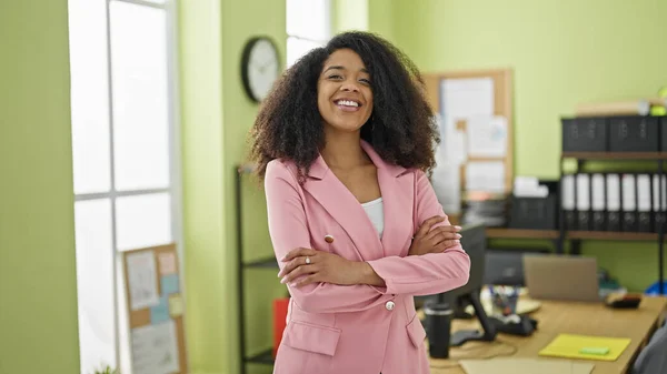 アフリカ系アメリカ人女性ビジネスワーカー笑顔自信を持って立ってとともに腕交差ジェスチャーでオフィス — ストック写真