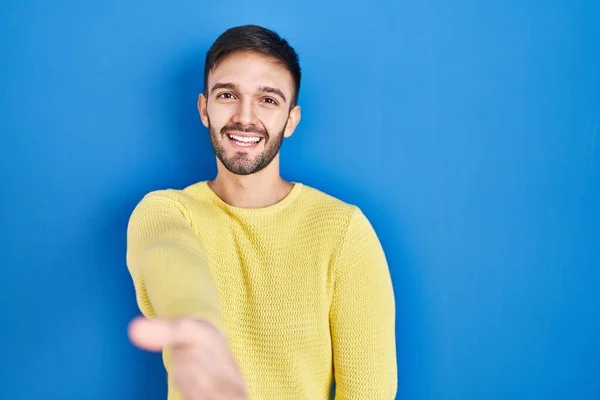 Hispanic Man Standing Blue Background Smiling Friendly Offering Handshake Greeting — Stockfoto