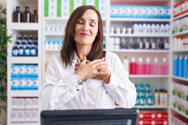 薬局で働く中年のブルネットの女性は 目を閉じて胸の上で手で笑顔で 顔に感謝のジェスチャー 健康の概念 — ストック写真
