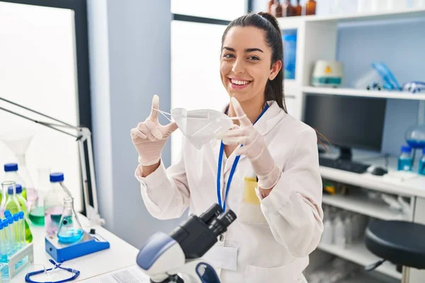 Young Beautiful Hispanic Woman Scientist Smiling Confident Holding Medical Mask — Stok fotoğraf