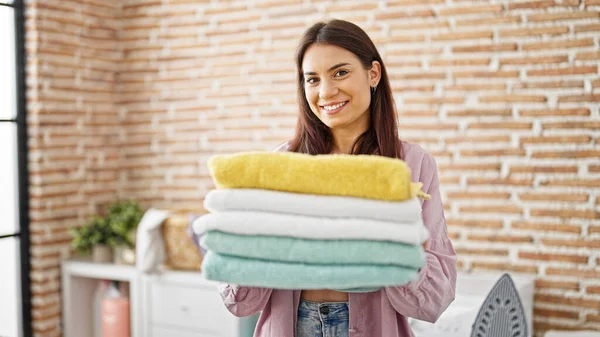 年轻美丽的惊慌失措的女人微笑着 自信地拿着折叠的毛巾在洗衣房里 — 图库照片