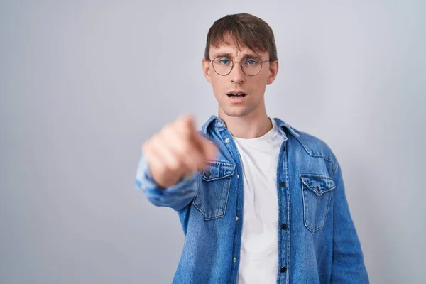 Caucasian blond man standing wearing glasses pointing displeased and frustrated to the camera, angry and furious with you