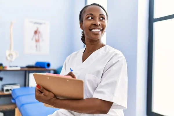 Femme Afro Américaine Physiothérapeute Souriant Confiant Écrire Rapport Médical Clinique — Photo