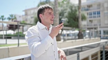 Beyaz bir adam sokakta akıllı telefonuyla sesli mesaj yolluyor.