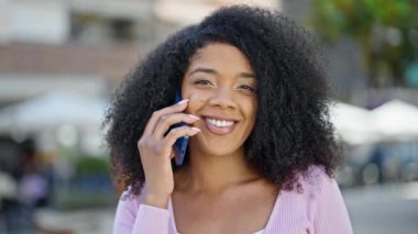 Afro-Amerikalı kadın gülümsüyor. Akıllı telefondan konuşuyor.