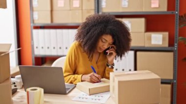 Afrikalı Amerikalı kadın ekommerce işçisi. Ofisteki pakette akıllı telefon yazısıyla konuşuyor.