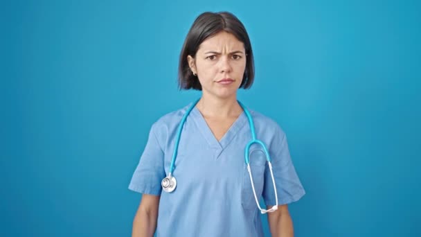 年轻美丽的惊慌失措的女医生严肃地站在那里 对着孤立的蓝色背景做着等待的姿势 — 图库视频影像