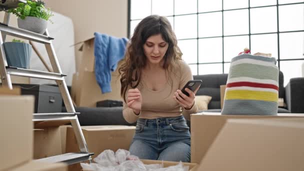 Young Beautiful Hispanic Woman Using Smartphone Unpacking Cardboard Box New — Stockvideo