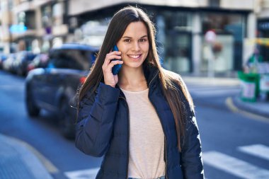 Genç, güzel, İspanyol bir kadın gülümsüyor ve caddede akıllı telefondan konuşuyor.