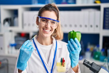 Laboratuvarda sebzelerle çalışan genç İspanyol kadın kameraya seksi bir ifadeyle bakıyor, neşeli ve mutlu bir yüzle.. 