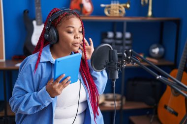 African american woman artist singing song holding touchpad at music studio