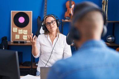 Man and woman musicians listening to music speaking at music studio