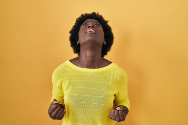 African young woman standing over yellow studio angry and mad screaming frustrated and furious, shouting with anger. rage and aggressive concept. 