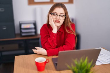 Young redhead woman business worker tired sitting on table at office