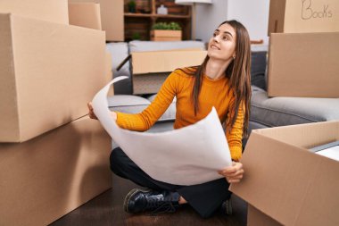 Genç beyaz kadın mimar yeni evinde kendine güvenen okuma evinin planlarını okuyor.