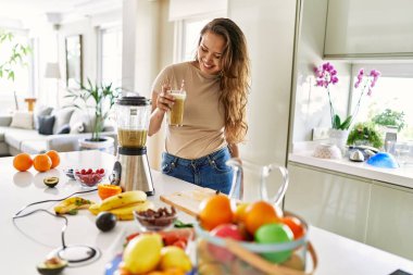 Genç ve güzel İspanyol kadın gülümsüyor. Mutfakta elinde bir bardak sebze suyu tutuyor.