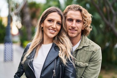 Kadın ve erkek gülümsüyor. Parkta birbirlerine sarılıyorlar.