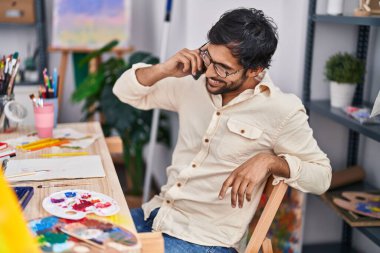 Young hispanic man artist smiling confident talking on the smartphone at art studio