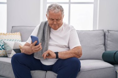 Orta yaşlı, kır saçlı, akıllı telefon kullanan, eve bakan bir adam.