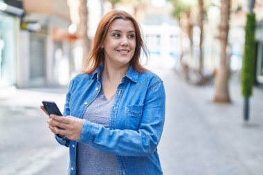 Young beautiful plus size woman smiling confident using smartphone at street