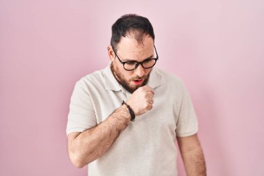 Artı, pembe arka planda sakallı İspanyol bir adam kendini iyi hissetmiyor ve soğuk algınlığı veya bronşitin belirtisi olarak öksürüyor. sağlık hizmeti kavramı. 