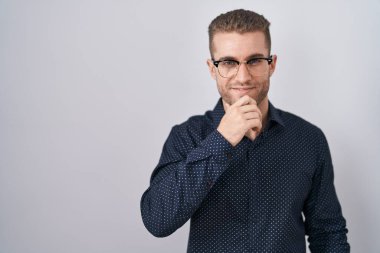 İzole edilmiş arka planda duran genç beyaz adam kameraya kollarını kavuşturup gülümseyerek ve çenesini kaldırarak bakıyor. Olumlu düşünmek. 