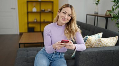 Evdeki kanepede oturan akıllı telefon kullanan genç, güzel İspanyol kadın.