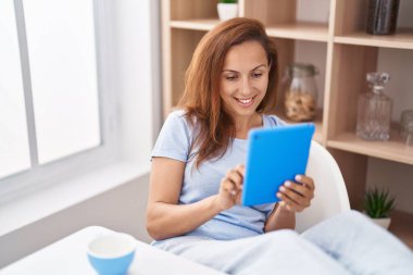 Young woman using touchpad and drinking coffee at home