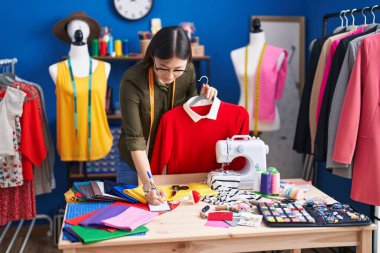 Chinese woman tailor holding shirt writing on paper at sewing studio