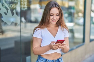 Sokakta akıllı telefon kullanan, kendine güvenen genç sarışın kadın.