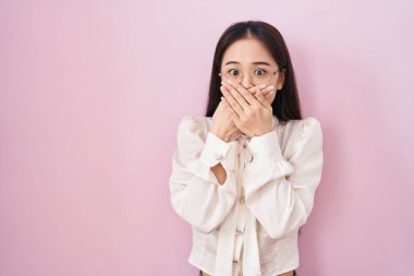 Pembe arka planda duran genç Çinli kadın yanlışlıkla elleriyle ağzını kapatırken şok oldu. gizli kavram. 
