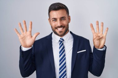 Yakışıklı İspanyol takım elbiseli ve kravatlı adam dokuz numaralı parmaklarını gösterip gösterirken kendinden emin ve mutlu gülümsüyor.. 