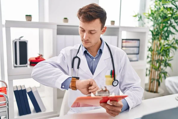 Młody Mężczyzna Lekarz Czytanie Raport Patrząc Zegarek Klinice — Zdjęcie stockowe