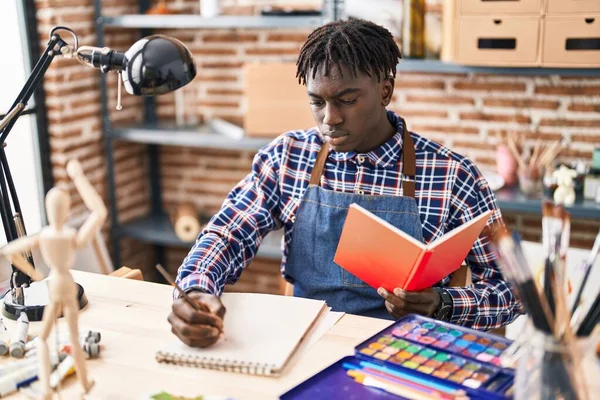 アフリカ系アメリカ人の男性アーティストがアートスタジオでノートを読む本を描く — ストック写真