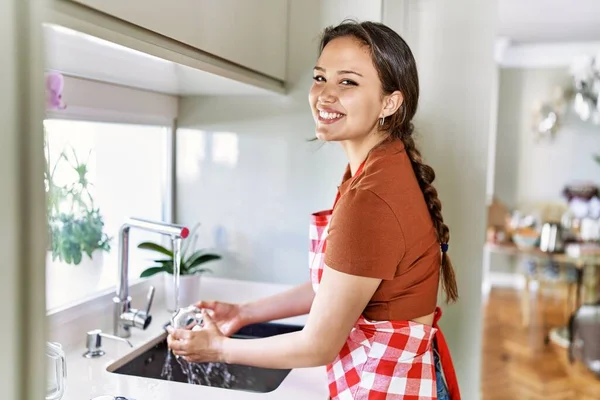 Young Beautiful Hispanic Woman Wearing Apron Washing Glass Kitchen — Stok fotoğraf
