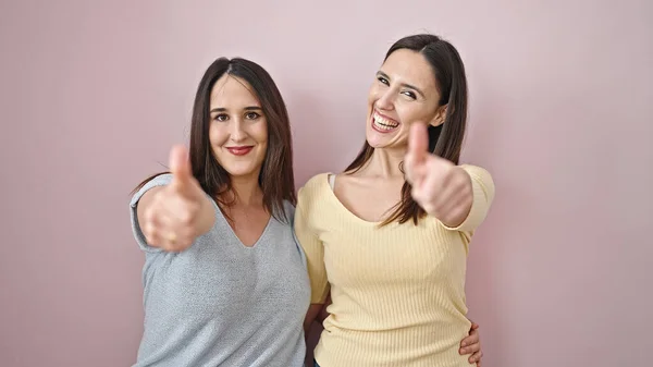 两个女人互相拥抱 用大拇指在孤立的粉色背景上做手势 — 图库照片