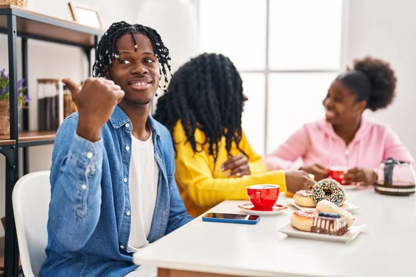 三个年轻的黑人坐在桌子上 手里拿着咖啡 大拇指指向旁边 笑着张开了嘴 — 图库照片