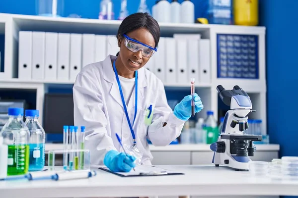 若いアフリカ系アメリカ人女性科学者は 実験室で血液検査管を保持する文書に書きます — ストック写真