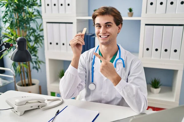 Young Doctor Man Holding Band Aid Smiling Happy Pointing Hand — Stock Photo, Image