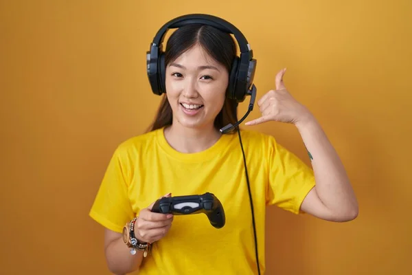 携帯電話で話すような手や指で携帯電話のジェスチャーをして笑顔コントローラーを持つビデオゲームをプレイしている中国の若い女性 コミュニケーションの概念 — ストック写真