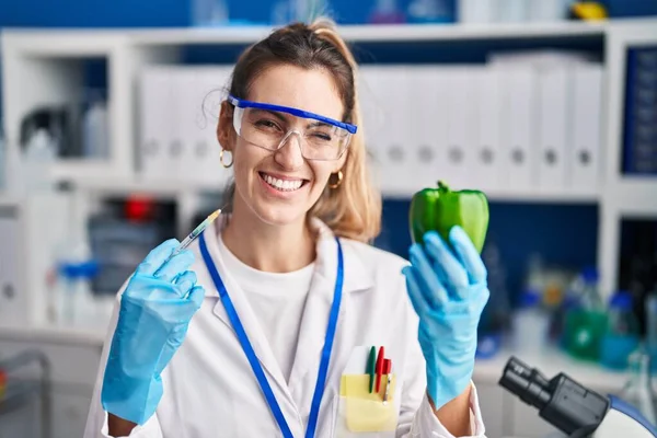 在科学家实验室工作的年轻而惊慌的女人带着蔬菜眨眼看着摄像机 脸上带着性感的表情 快乐的表情 — 图库照片