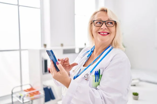 Middle Age Blonde Woman Wearing Doctor Uniform Using Smartphone Clinic — Stock Photo, Image